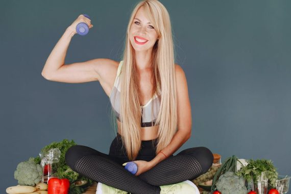 Woman lifting a small dumbbell while surrounded by fresh vegetables, embodying health and fitness.